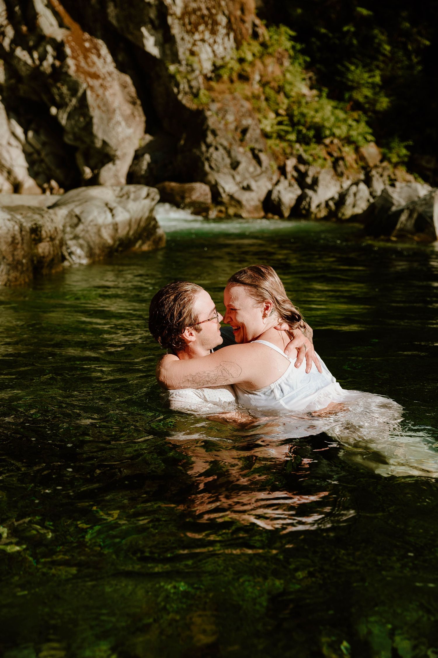 Two people embrace while swimming in crystal clear water near rocky cliffs.