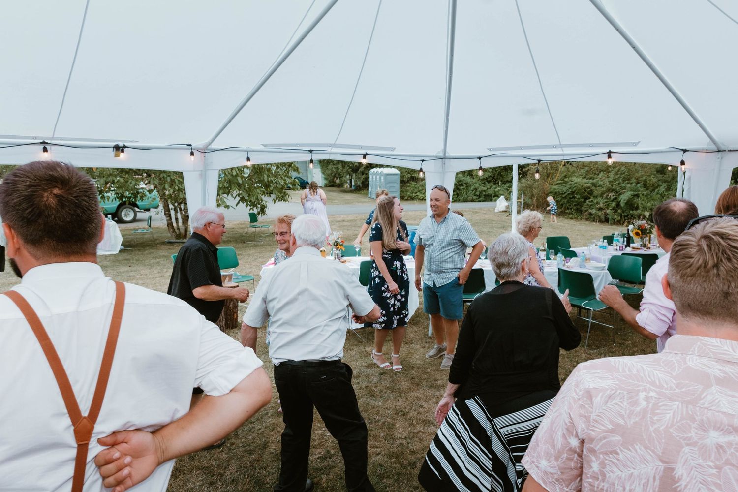 Wedding guests dance and celebrate under a white outdoor tent during a reception.