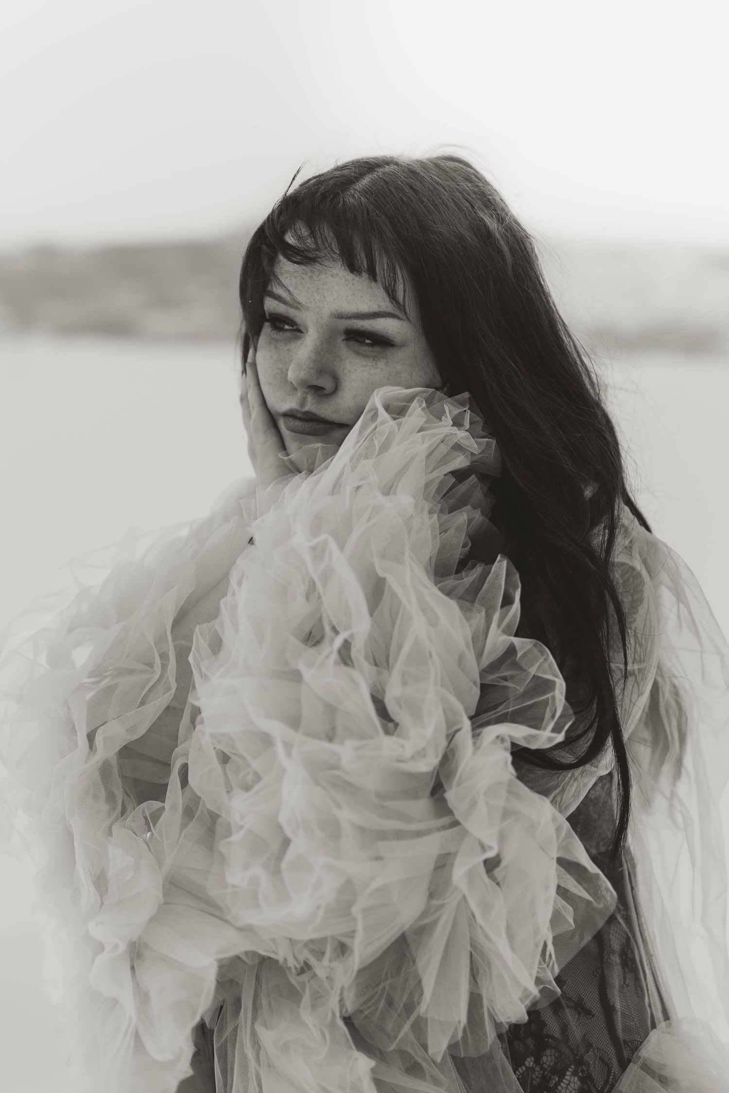 Dreamy black and white portrait of woman wrapped in flowing tulle fabric against a soft blurred background.
