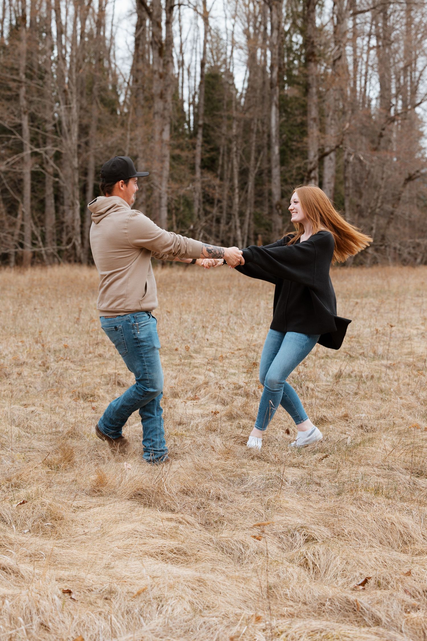 Couple dances playfully together in autumn field with trees in background.