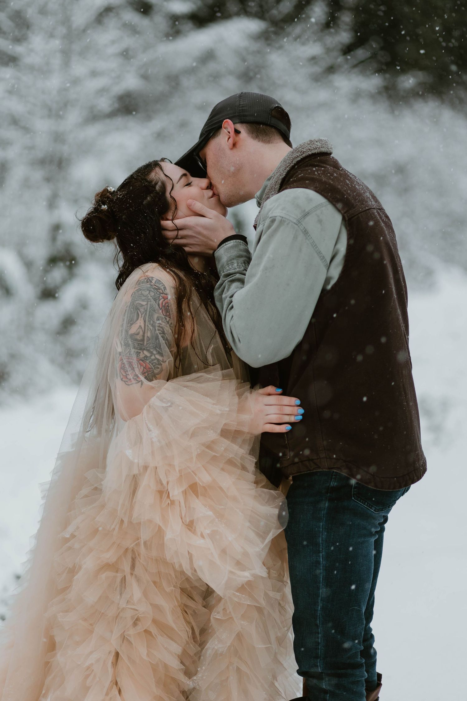 A romantic kiss shared in a snowy forest setting with a flowing blush gown.