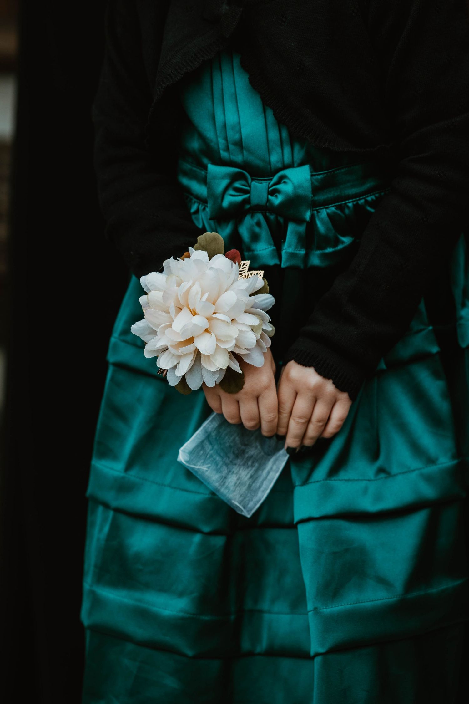 Close-up of hands holding a white flower against a teal ruffled dress.