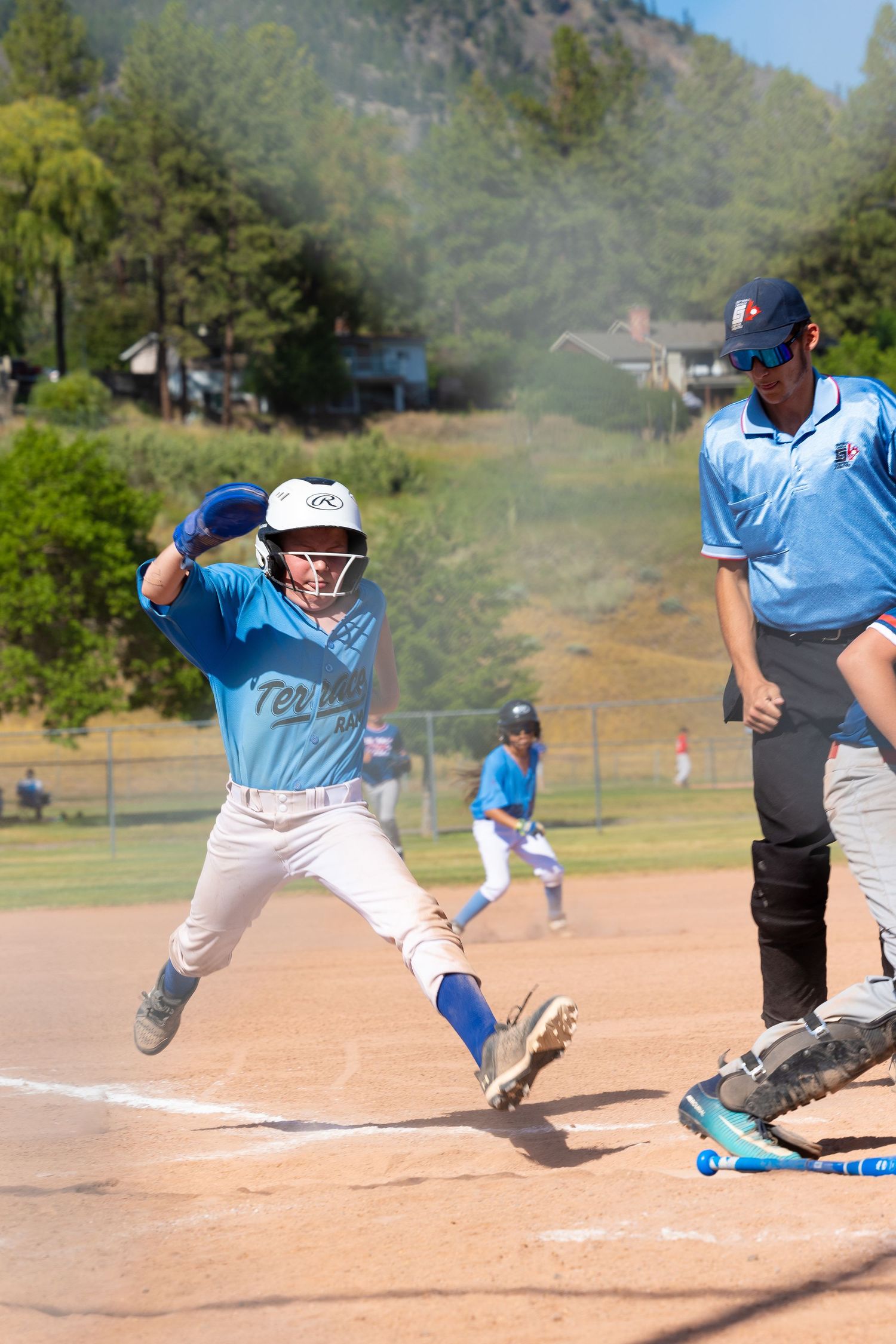 Youth baseball player sliding into base while umpire watches nearby.
