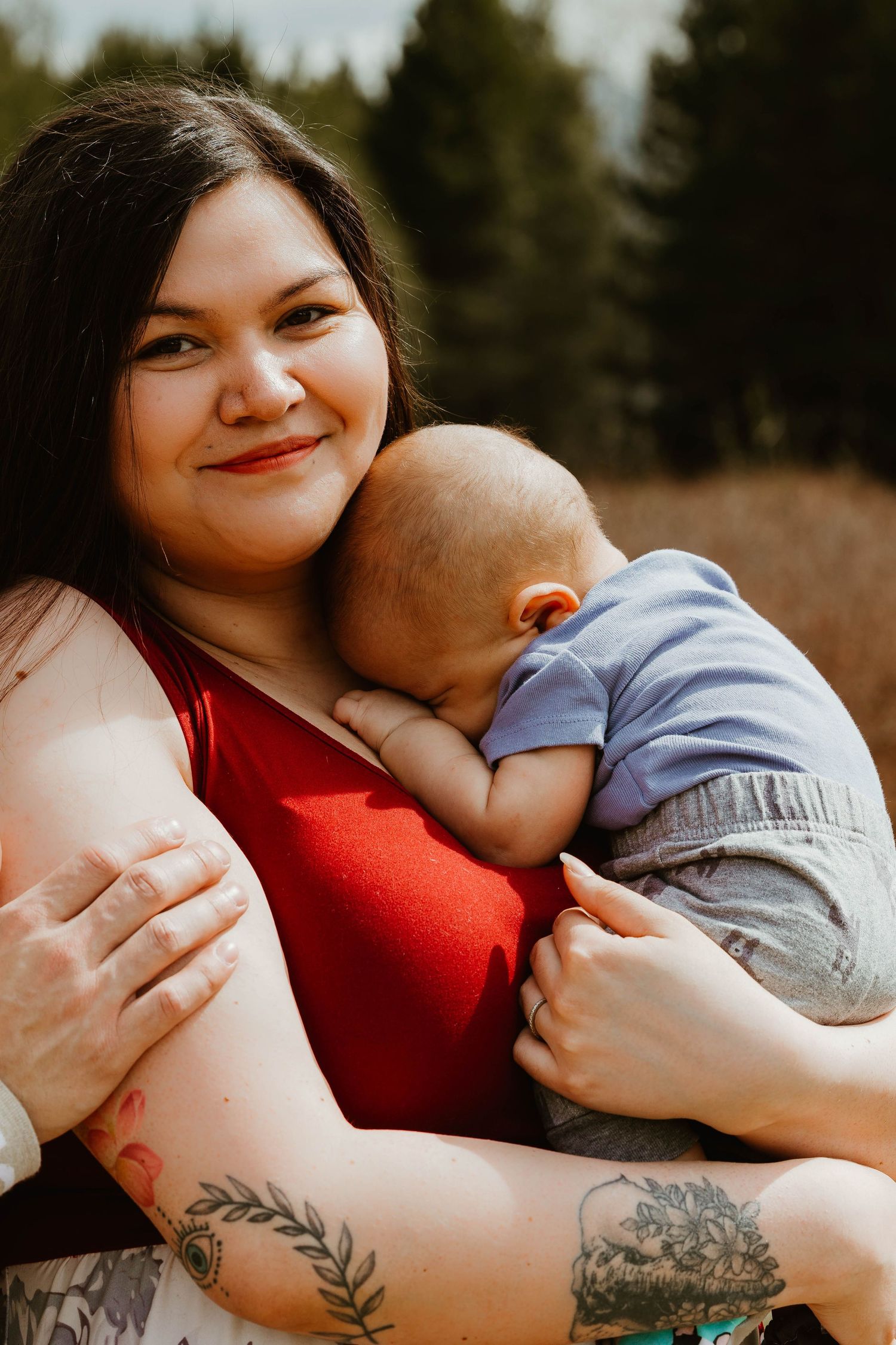 A tender moment between parent and sleeping baby in a sunny outdoor setting.