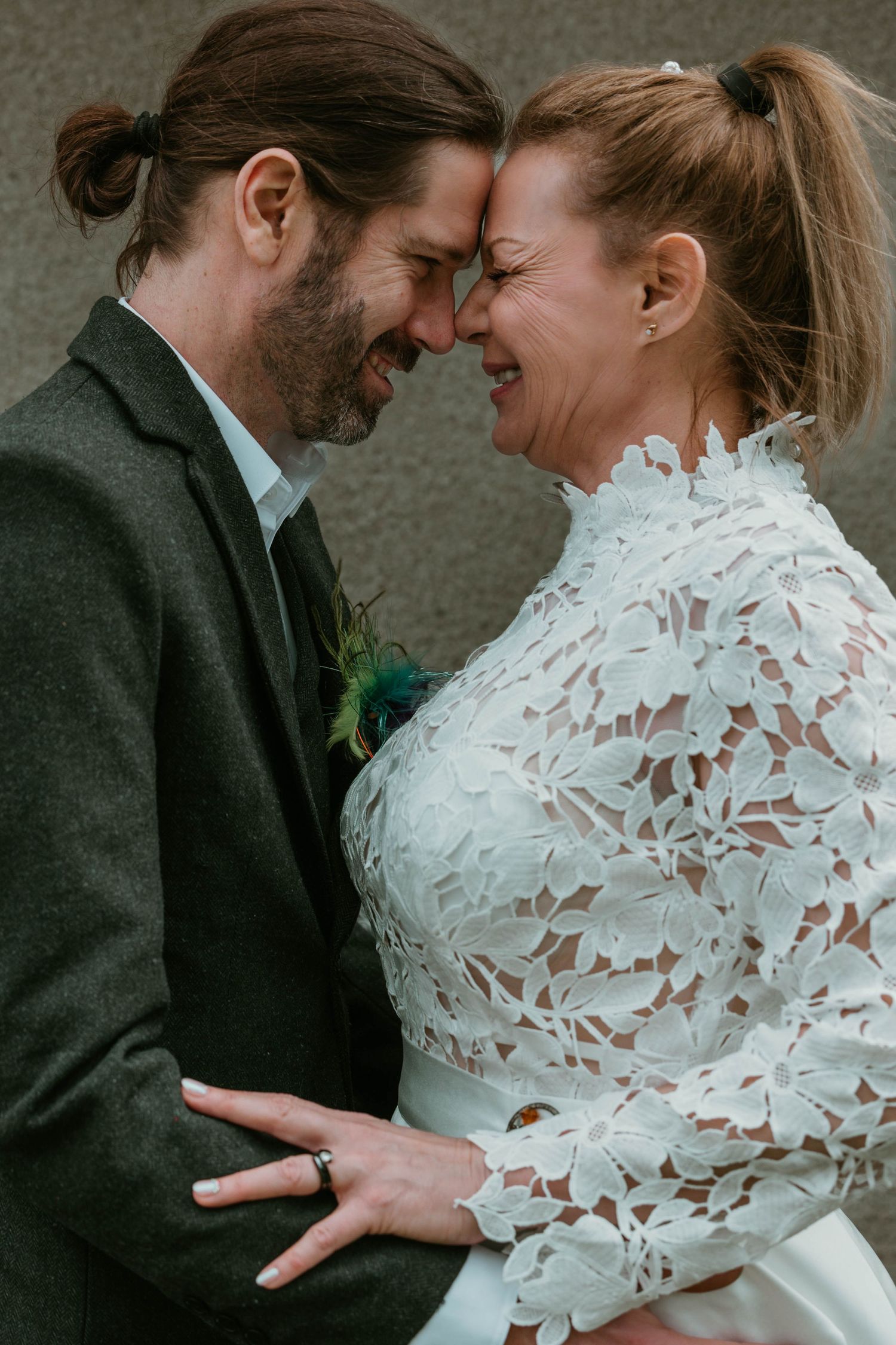 Intimate close-up of newlyweds sharing a tender moment against grey wall.