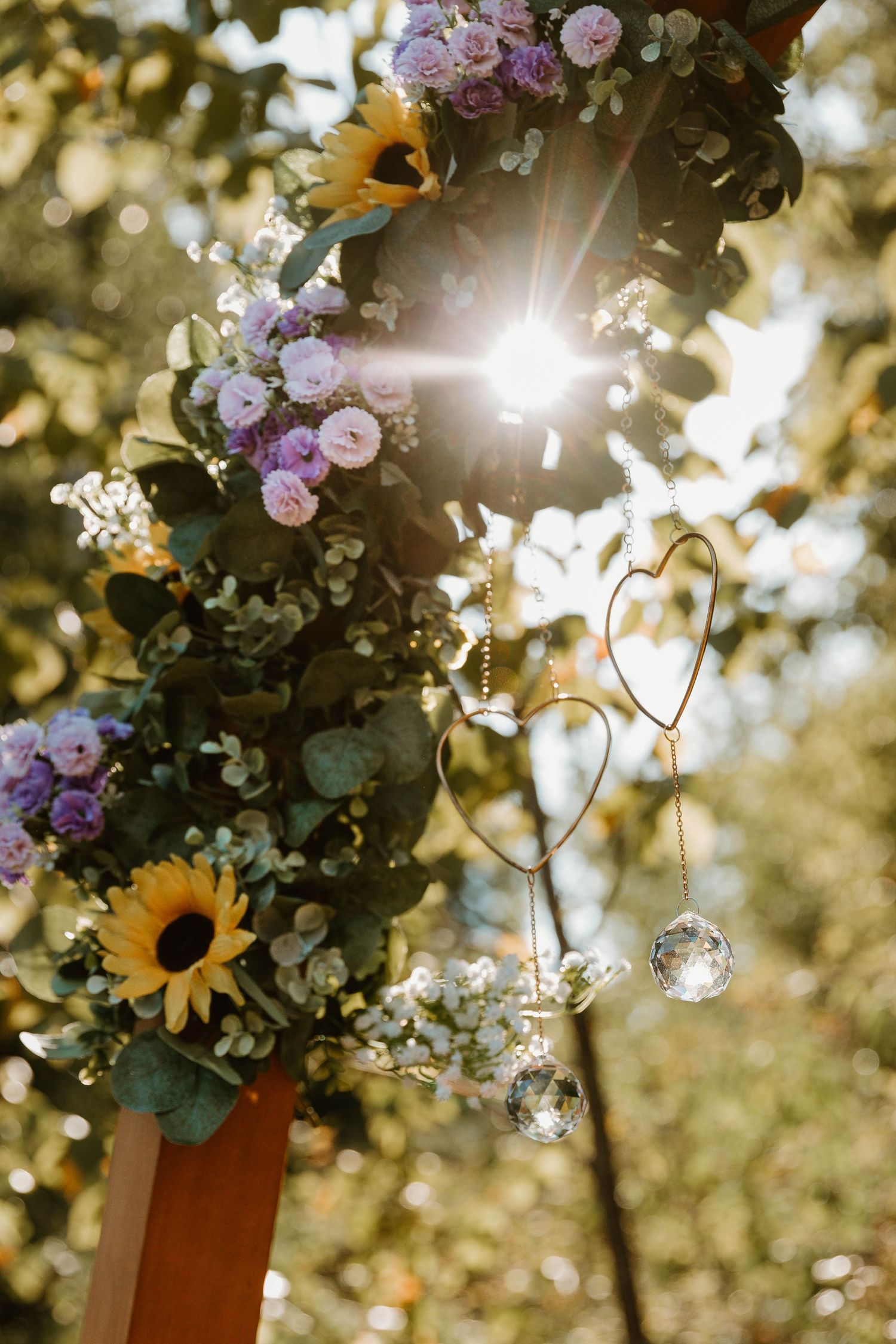 Floral wedding arch with sunflowers and purple blooms backlit by sunset.