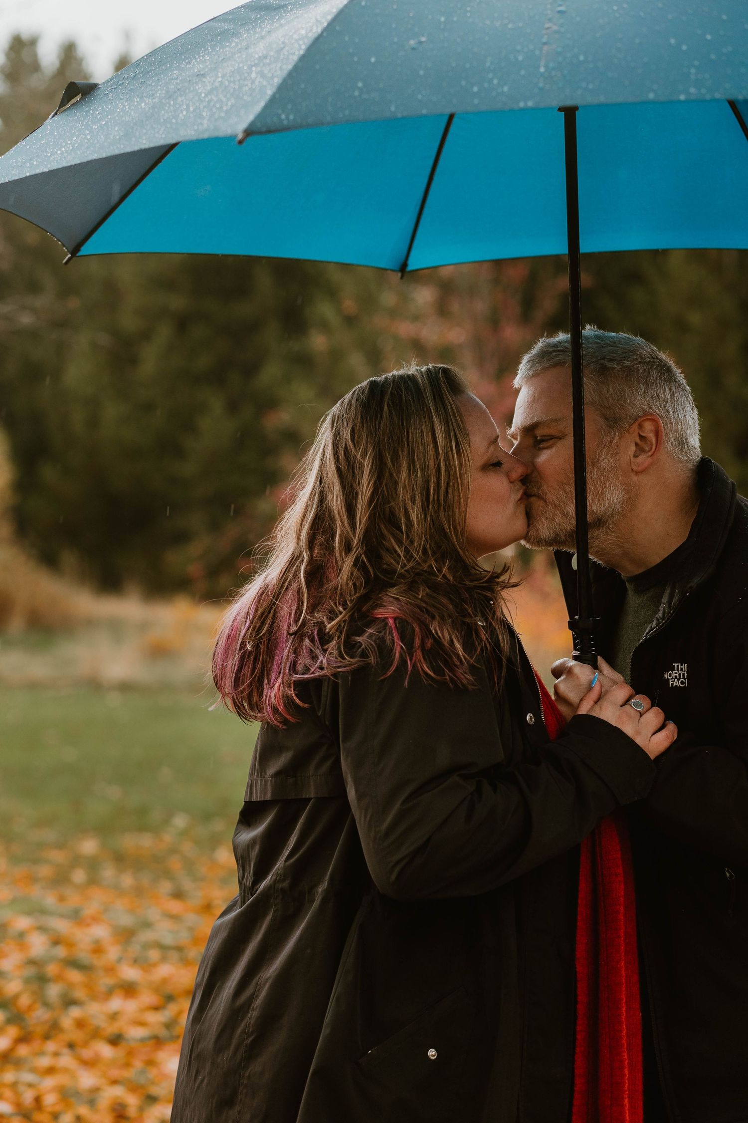 A romantic kiss shared under a bright blue umbrella during a misty autumn day.