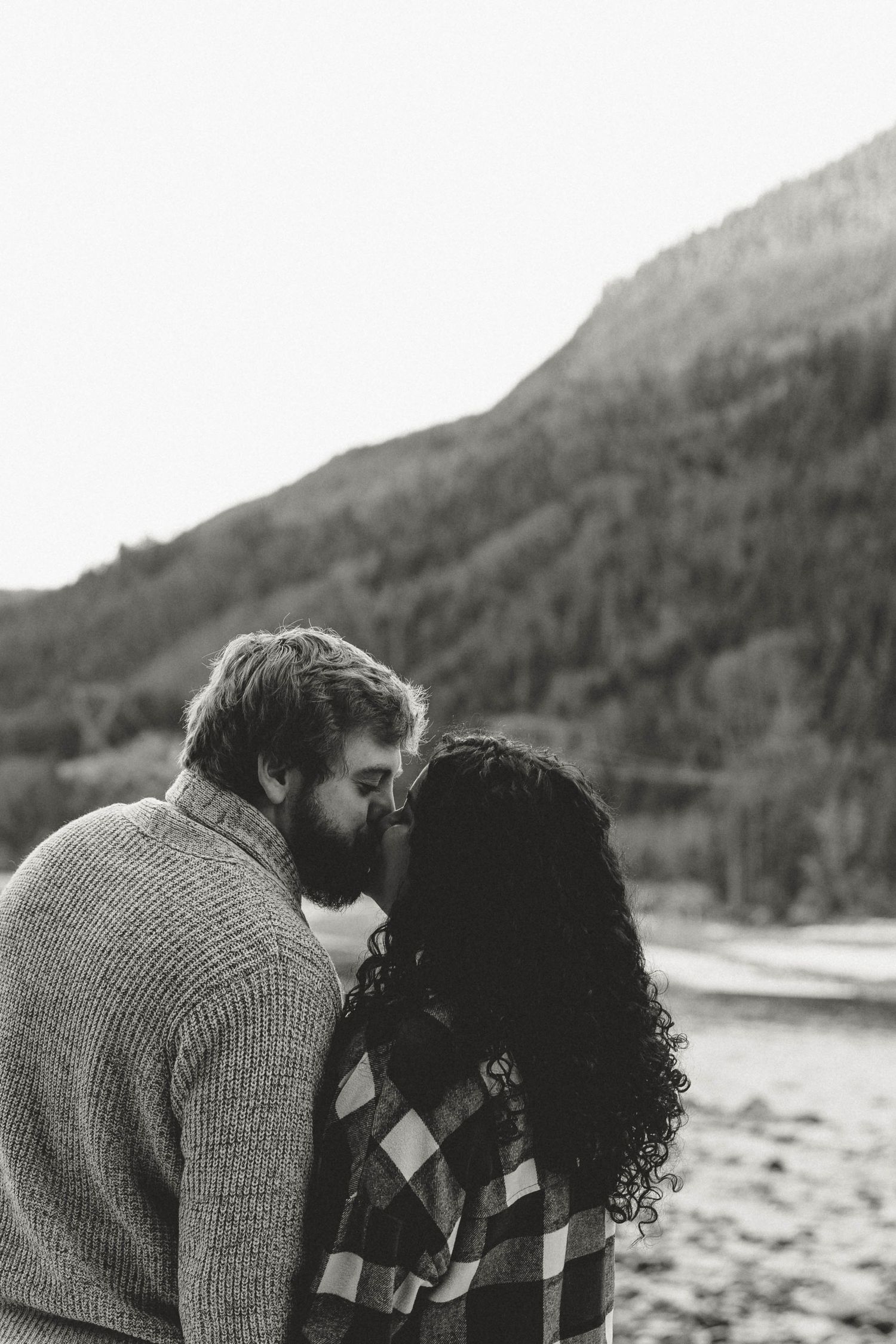 Black and white photo of a couple sharing an intimate moment by a mountain lake.