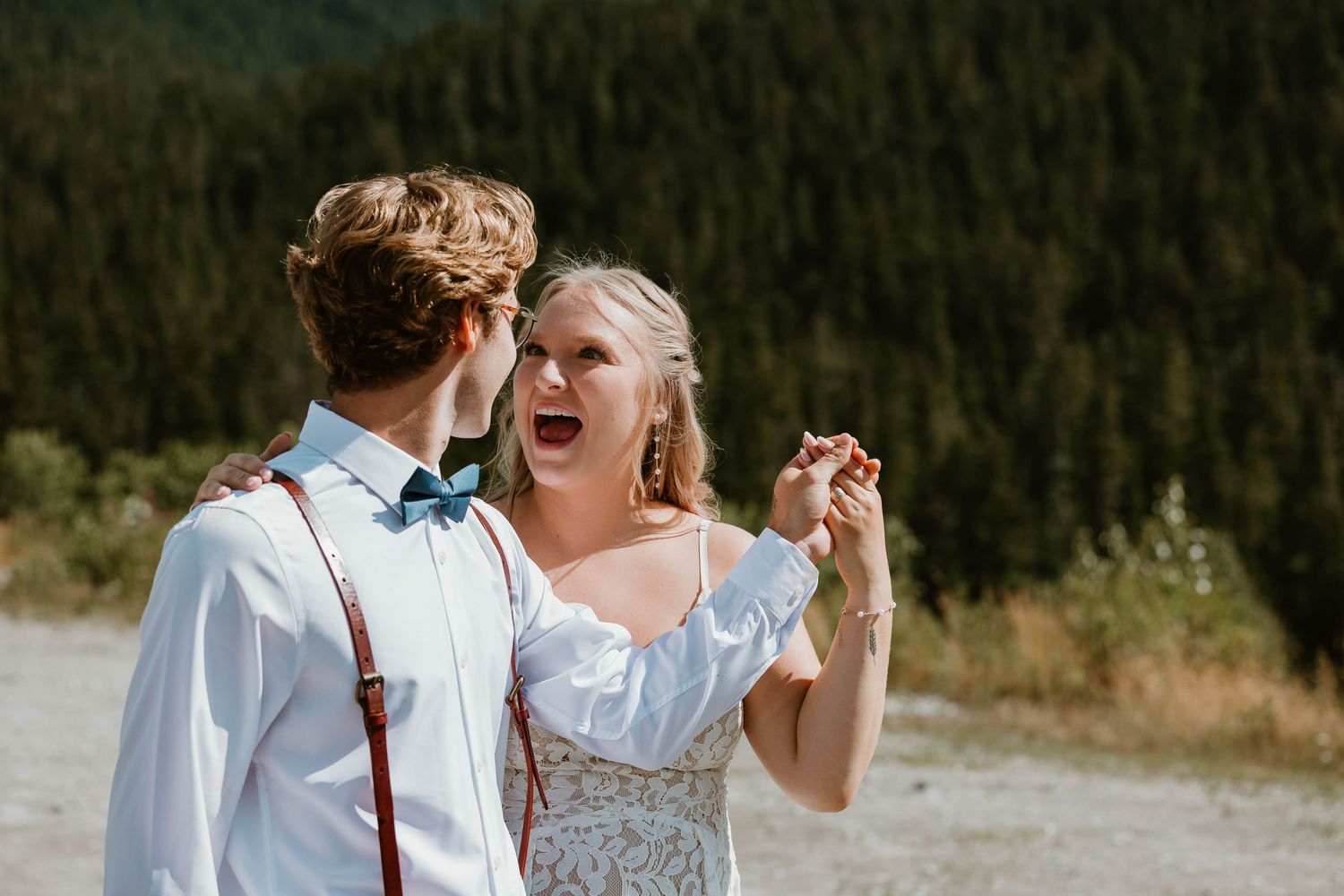 Joyful candid moment between couple in wedding attire against mountain vista.