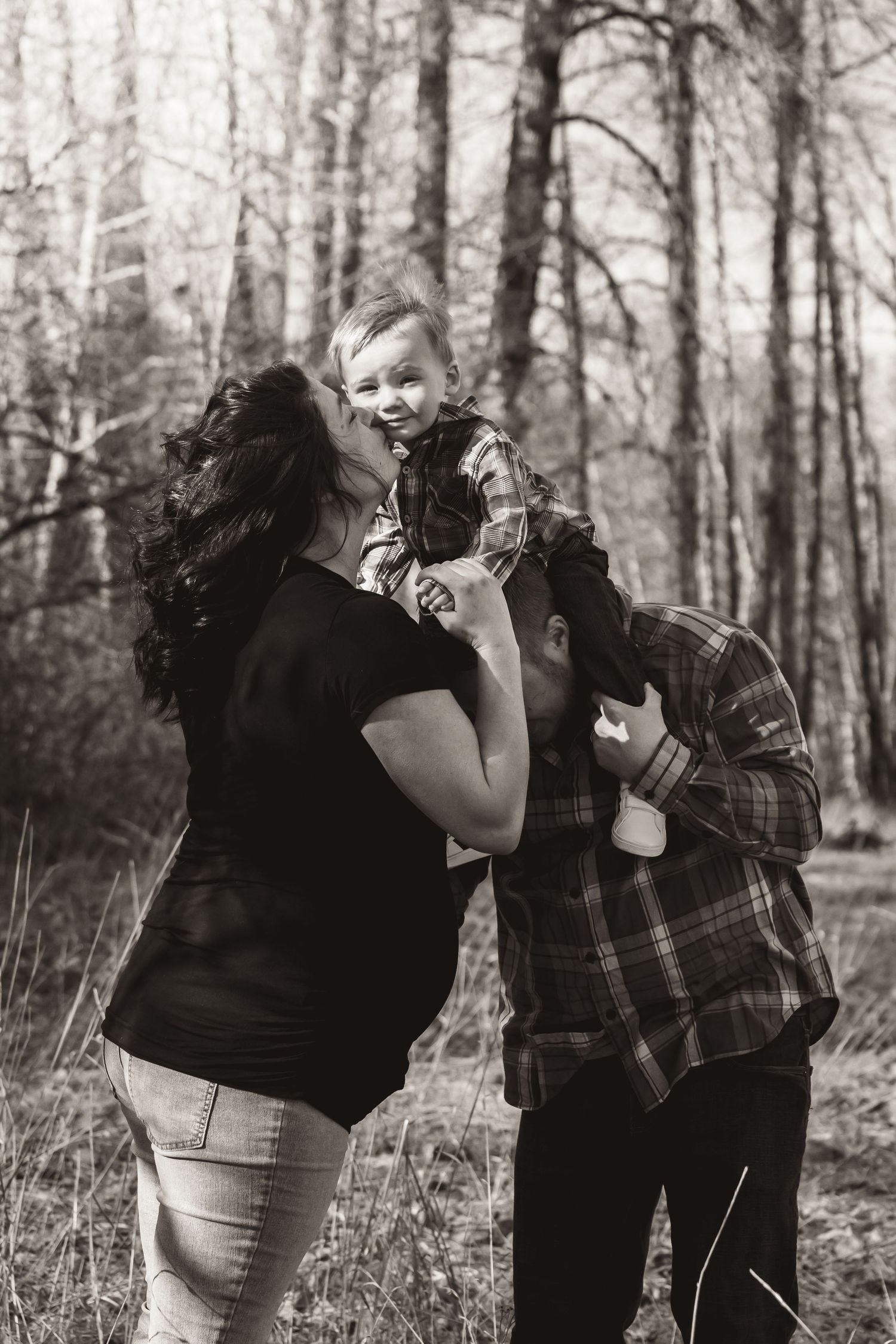 Black and white portrait of family members lifting and embracing child outdoors.