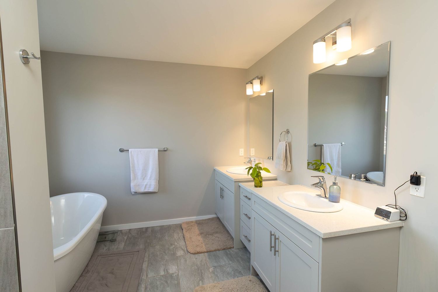 Modern master bathroom interior with white vanity cabinets, freestanding tub and gray tile floors.