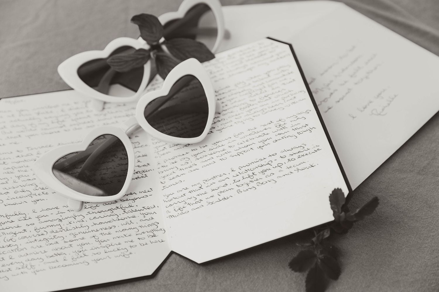 Black heart-shaped sunglasses rest on handwritten letters in a series of black and white photographs.