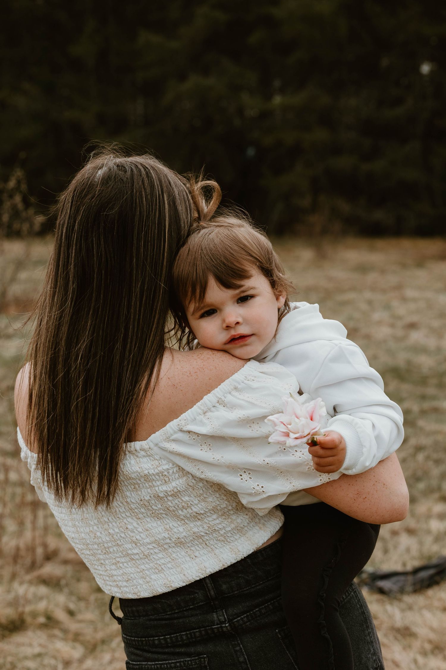 A tender moment between parent and child in white outfits against a natural outdoor backdrop.