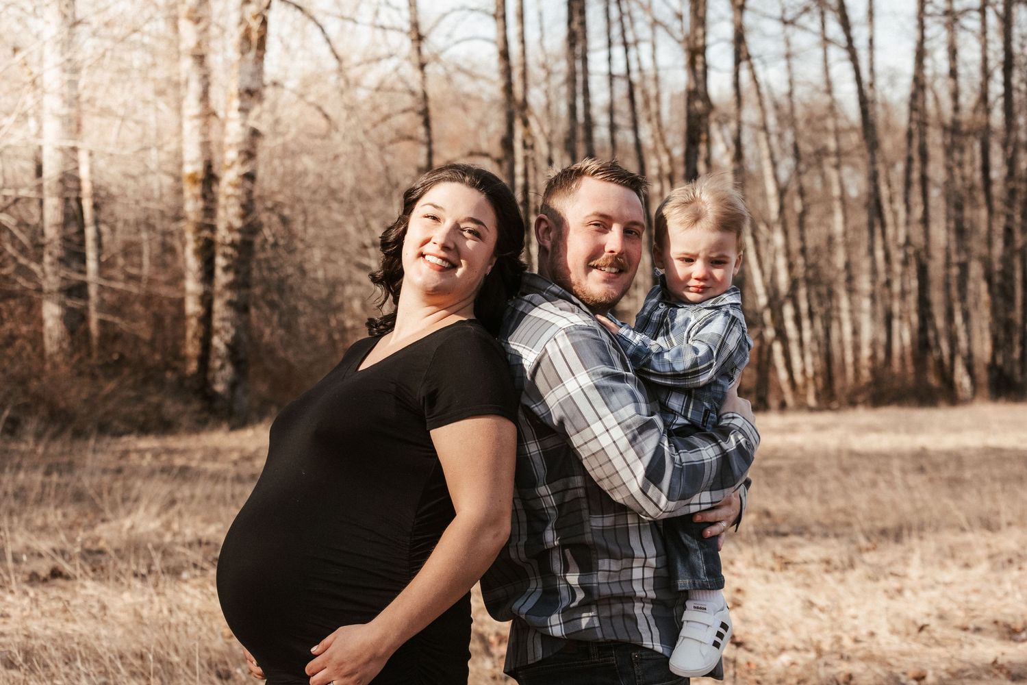 Family poses together in autumn field during sunset maternity session.