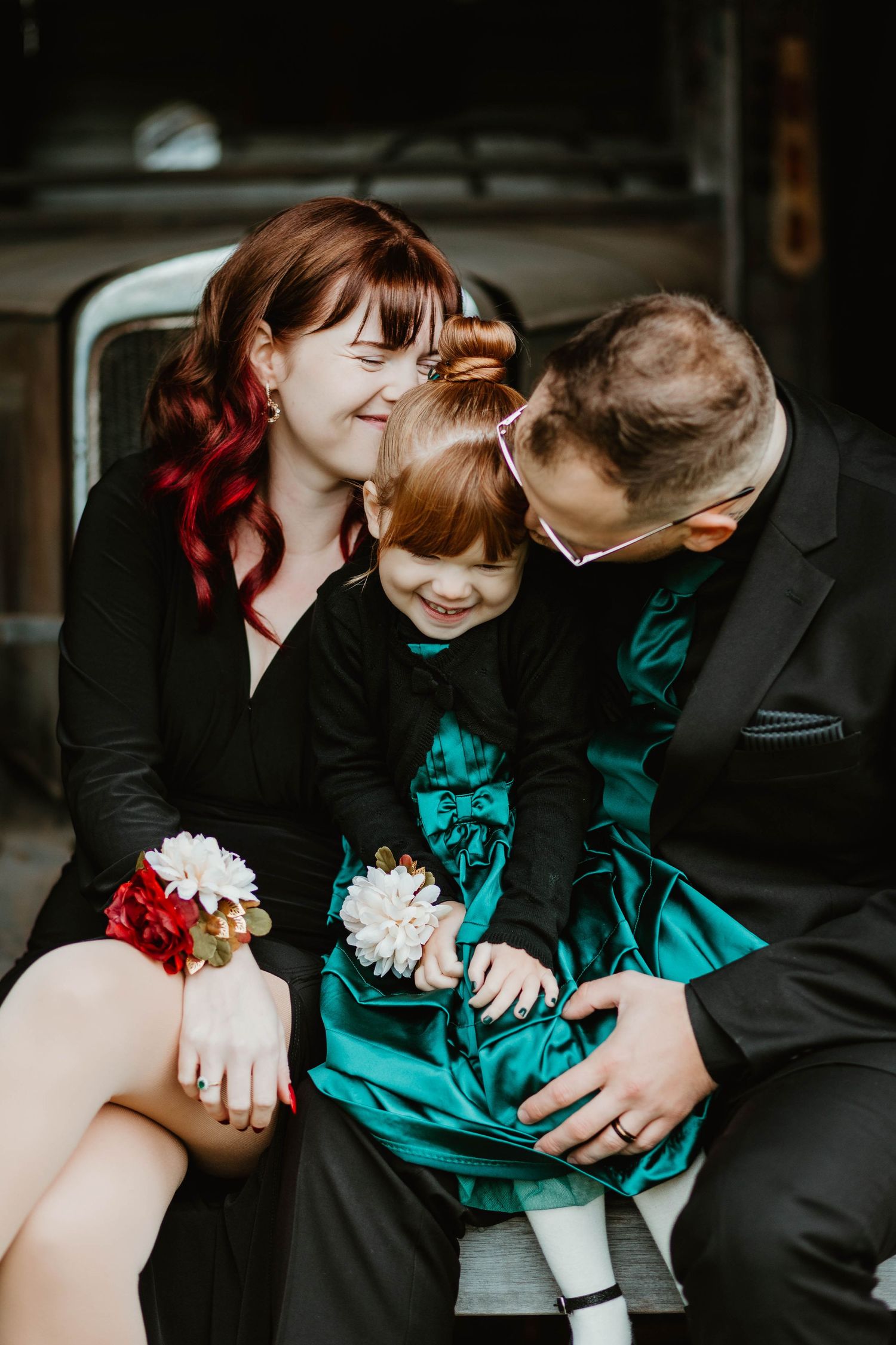 Intimate family portrait featuring coordinated black and teal outfits by vintage car.