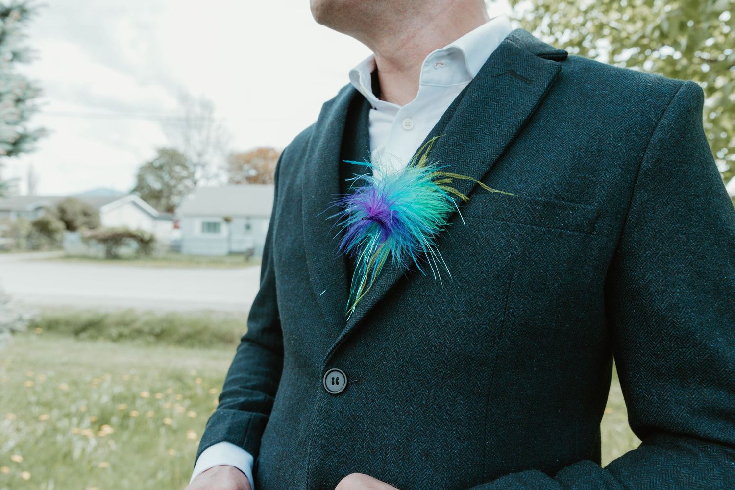 A close-up of a vibrant teal and purple feather boutonniere on a dark suit jacket.