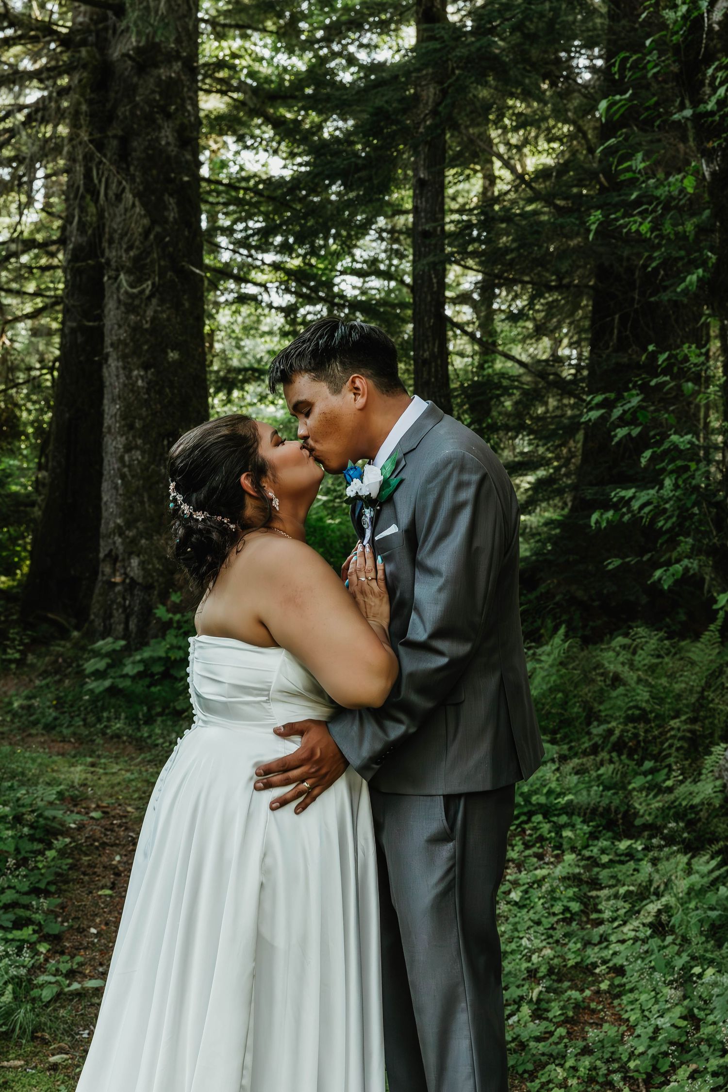 Newlyweds share a tender kiss on a forest path during their wedding.