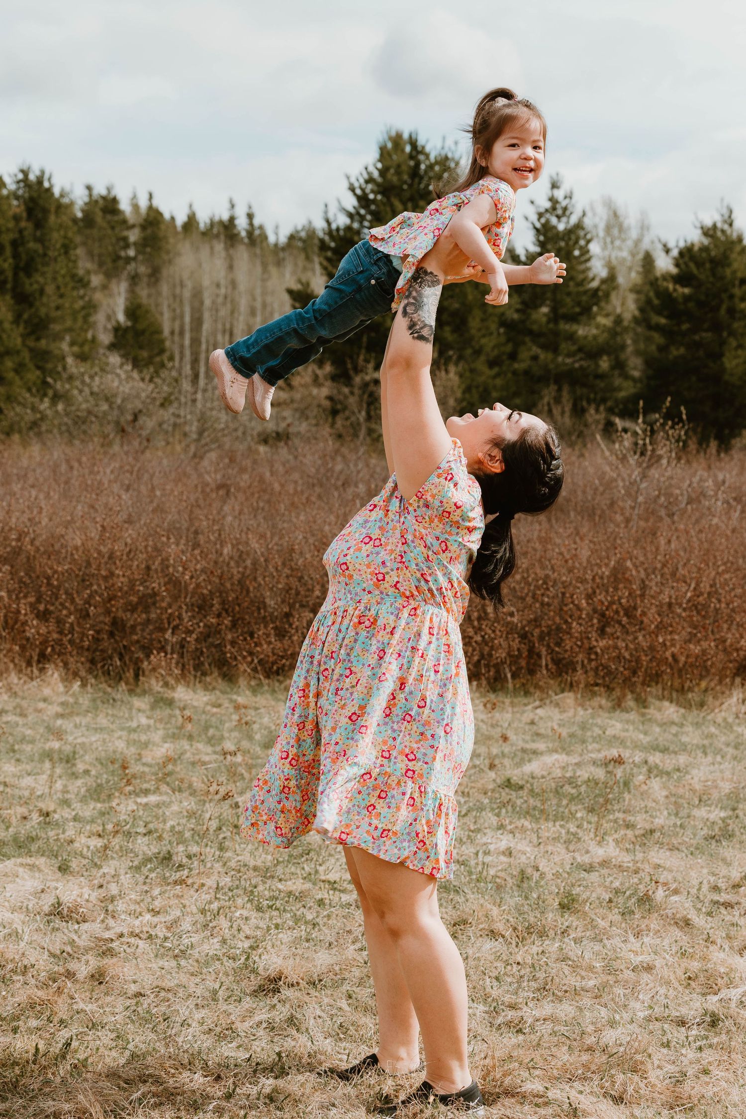 A joyful moment of play in an outdoor setting with a floral dress against a natural backdrop.