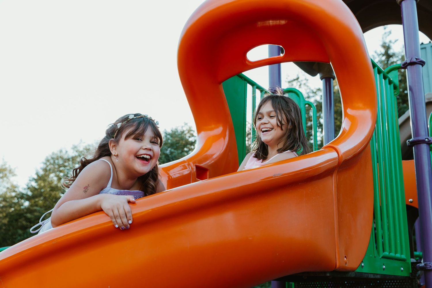 Children playing and laughing on bright orange playground slide.