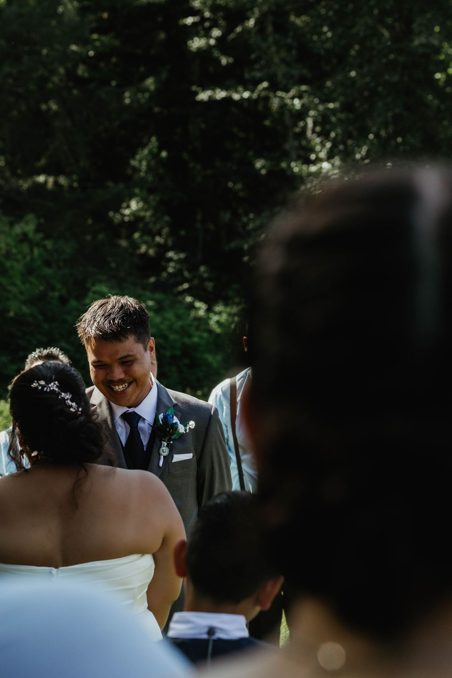 Joyful exchange during an outdoor wedding ceremony with natural forest backdrop.