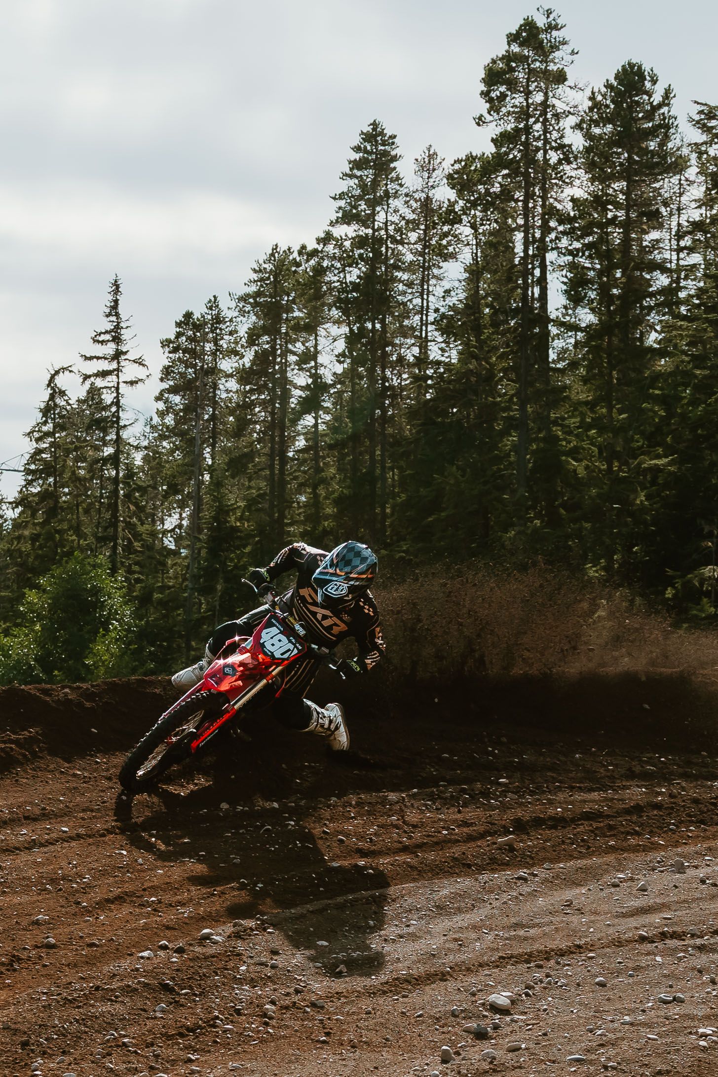 A sequence of dirt bike jumps showing a rider performing aerial tricks on a muddy forest trail.