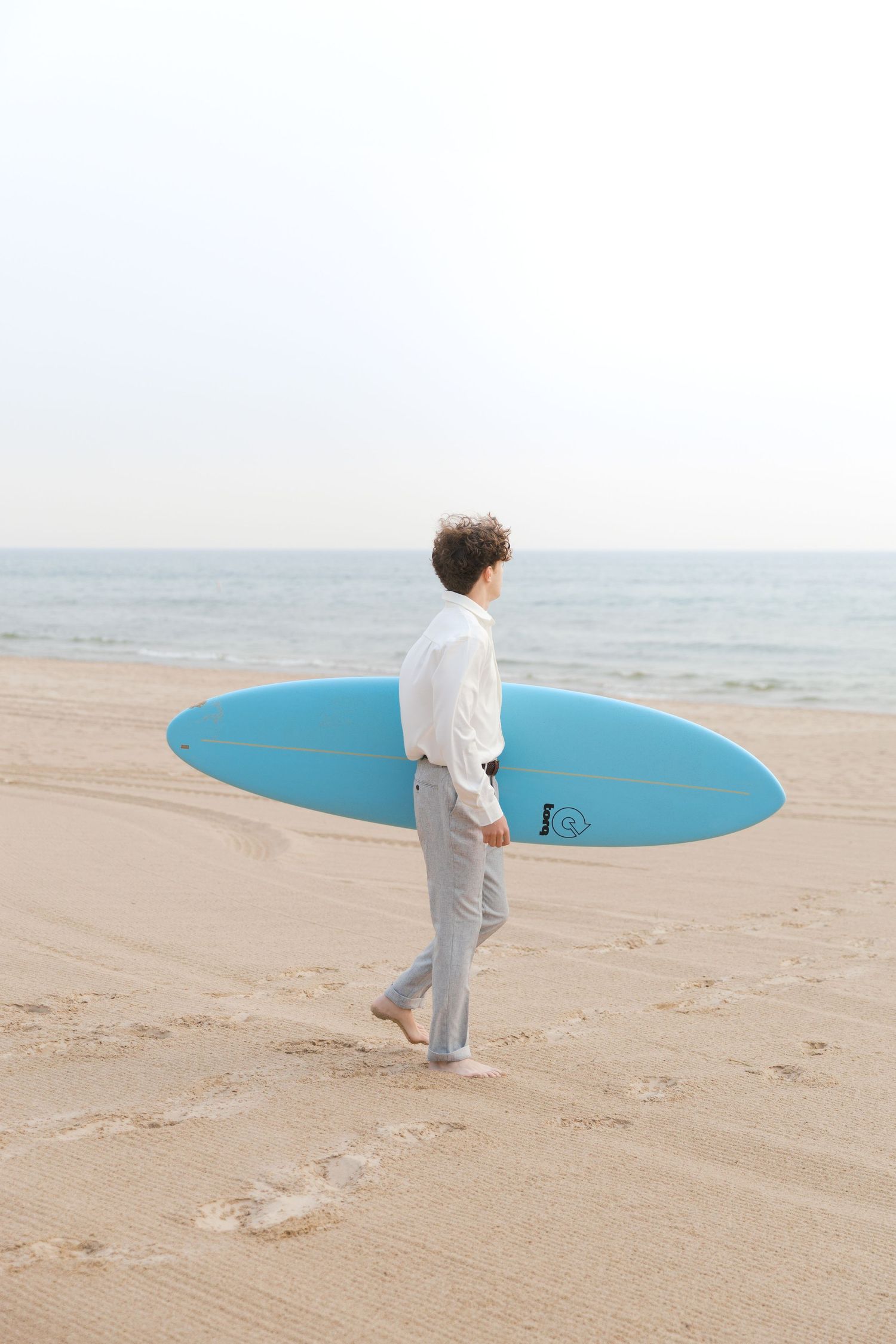 Grand Haven Lake Michigan Beach Senior Portrait Photoshoot. Sand dunes, beach grass, and the great lakes on the boardwalk with a surfboard