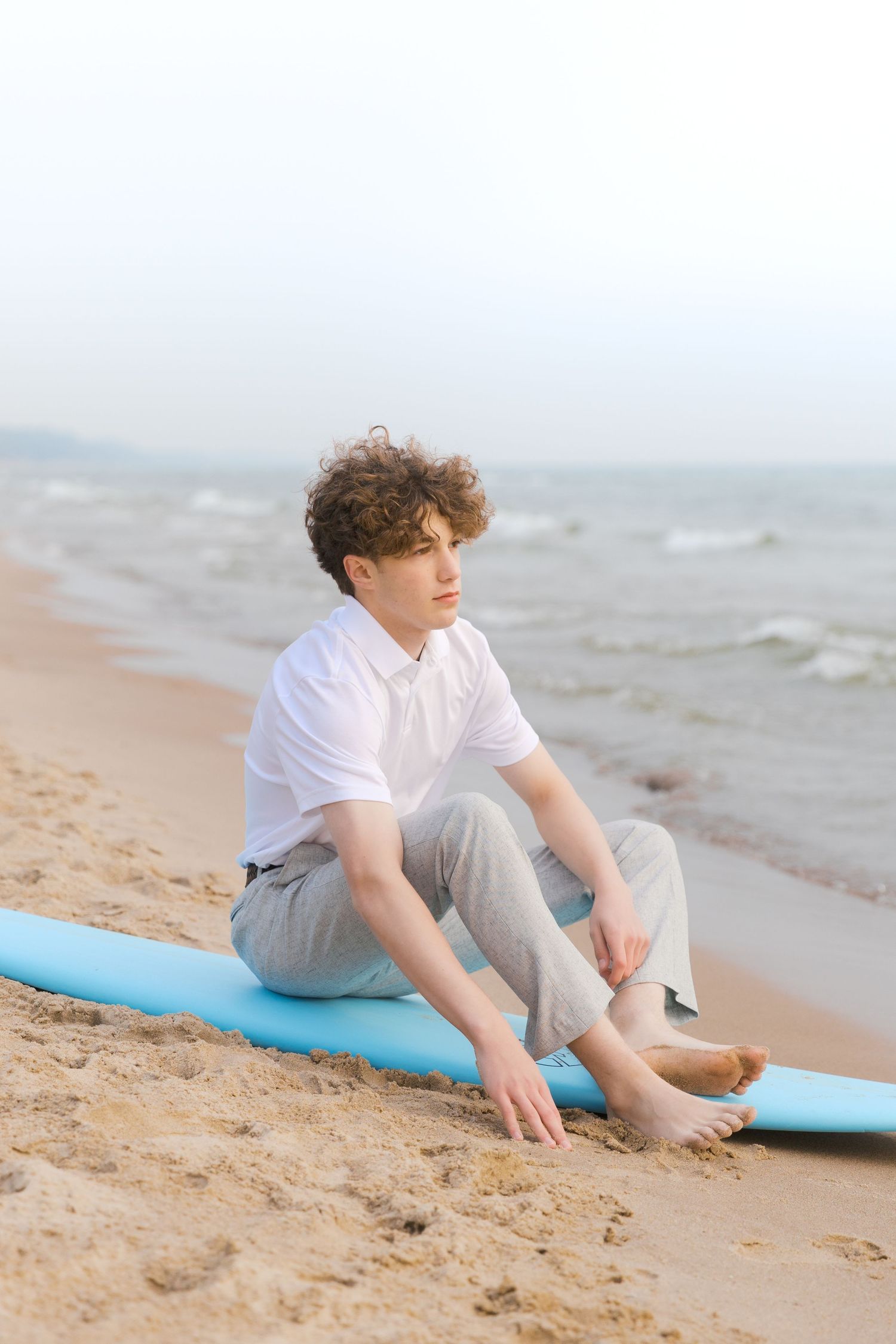 Grand Haven Lake Michigan Beach Senior Portrait Photoshoot. Sand dunes, beach grass, and the great lakes on the boardwalk with a surfboard