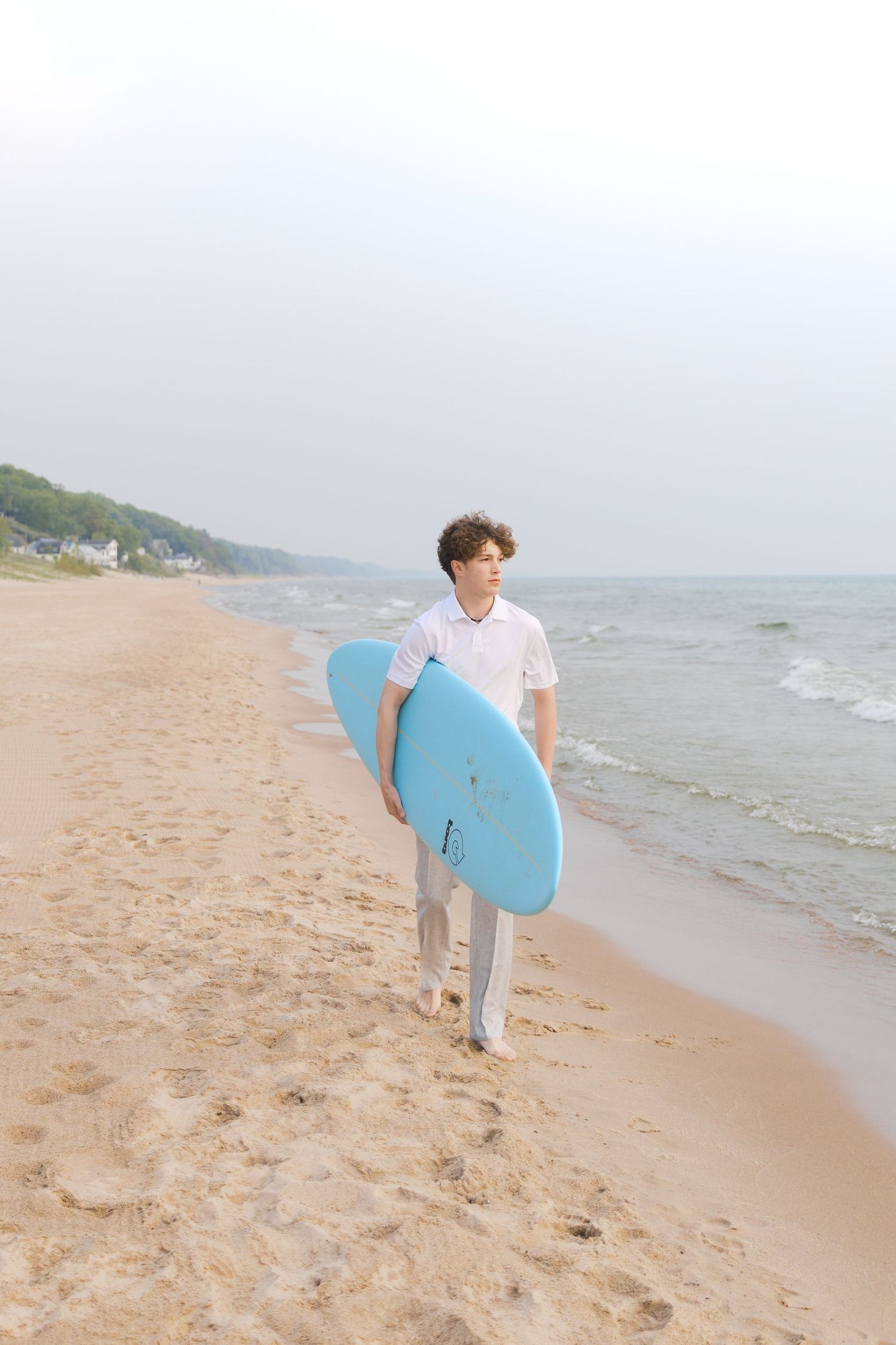 Grand Haven Lake Michigan Beach Senior Portrait Photoshoot. Sand dunes, beach grass, and the great lakes on the boardwalk with a surfboard