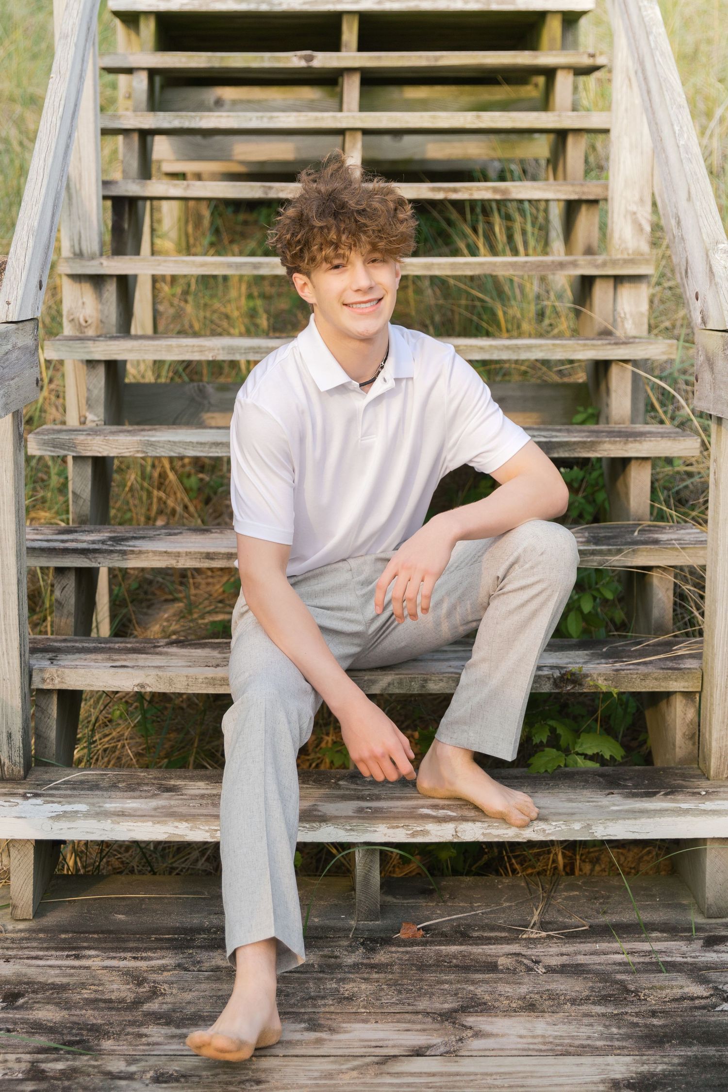 Grand Haven Lake Michigan Beach Senior Portrait Photoshoot. Sand dunes, beach grass, and the great lakes on the boardwalk with a surfboard