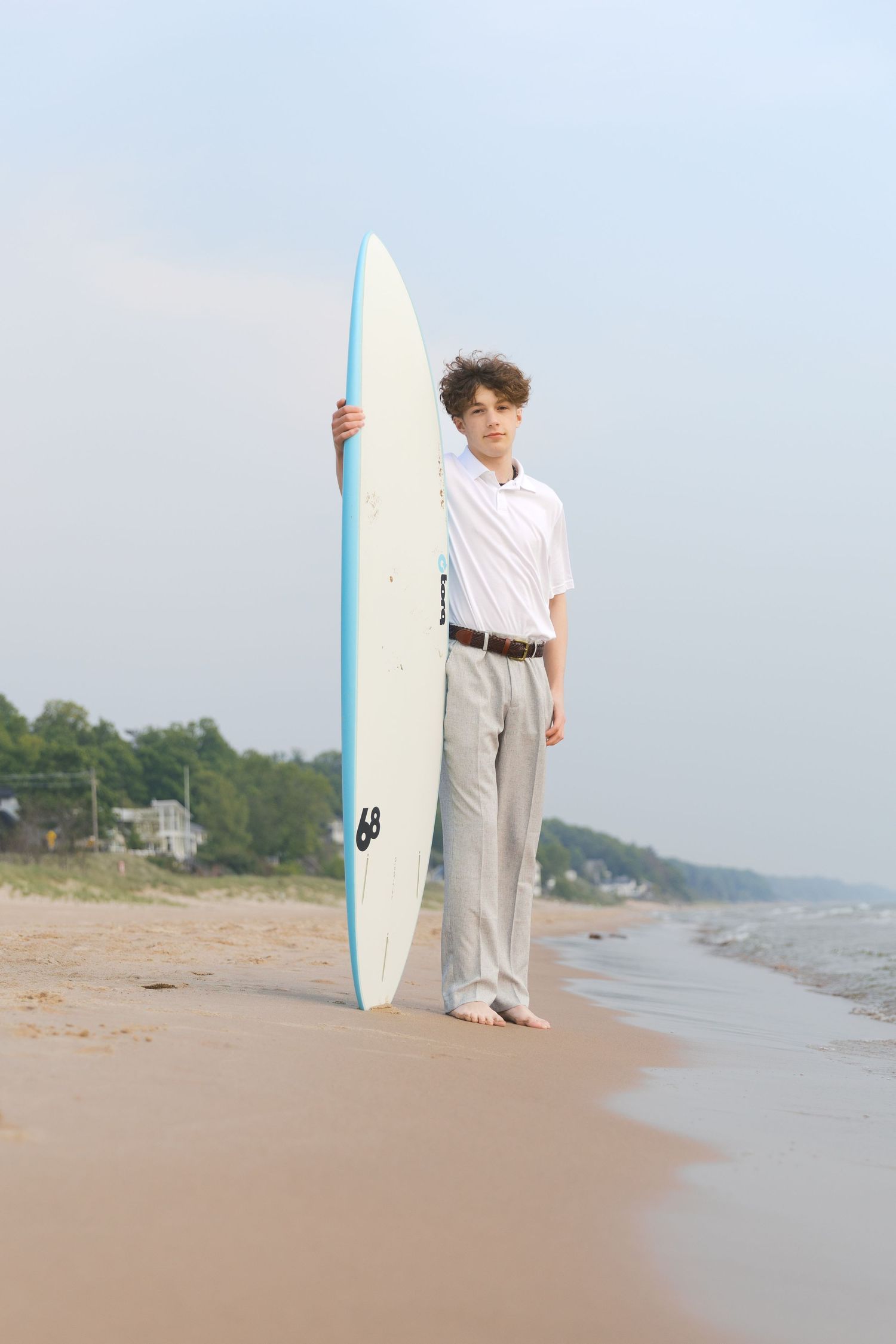 Grand Haven Lake Michigan Beach Senior Portrait Photoshoot. Sand dunes, beach grass, and the great lakes on the boardwalk with a surfboard