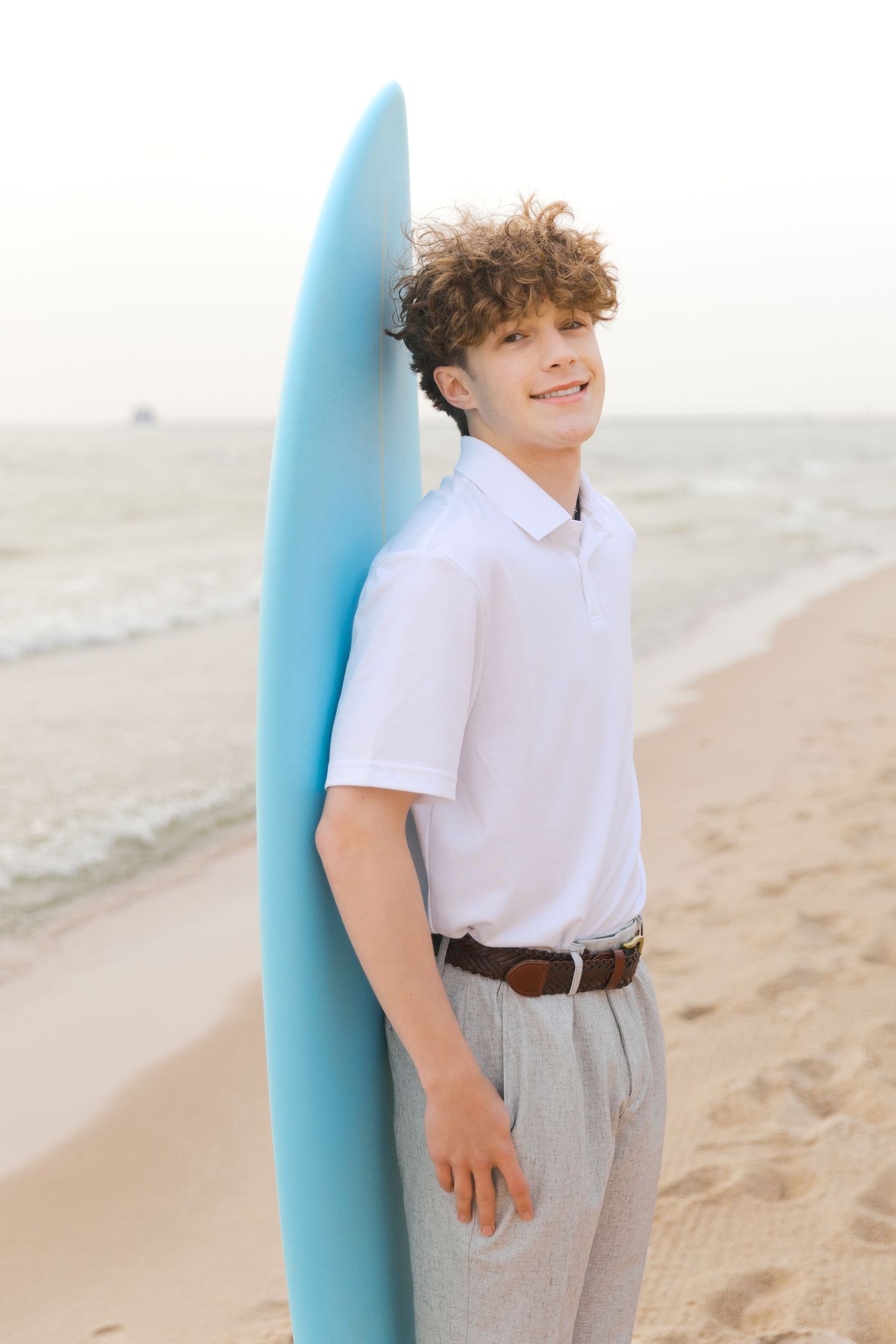 Grand Haven Lake Michigan Beach Senior Portrait Photoshoot. Sand dunes, beach grass, and the great lakes on the boardwalk with a surfboard