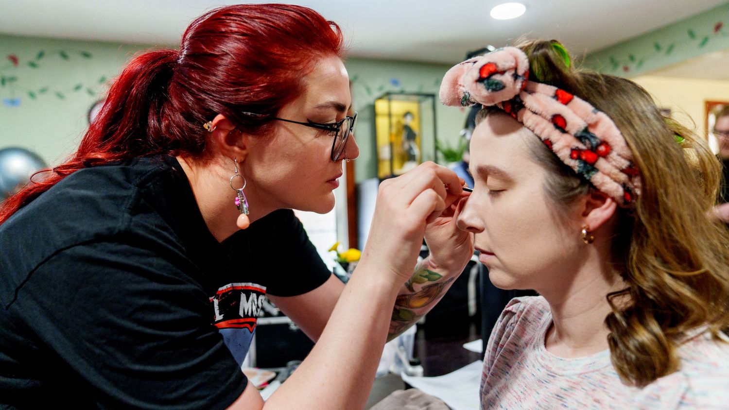 Professional makeup artist applying makeup to a young woman wearing a floral headband in a salon.