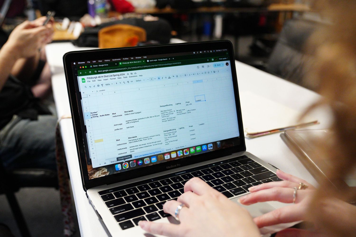 Person typing on a MacBook laptop displaying a spreadsheet in Google Sheets at a desk.