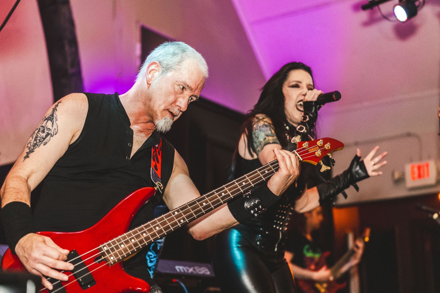 A rock band performs on stage with colorful purple lighting and energetic musicians playing instruments.