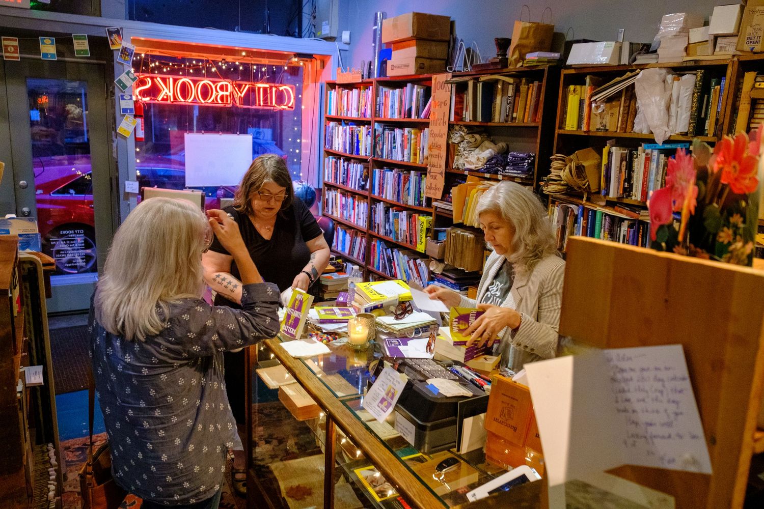 Customers browse books at an independent bookstore with neon signage.