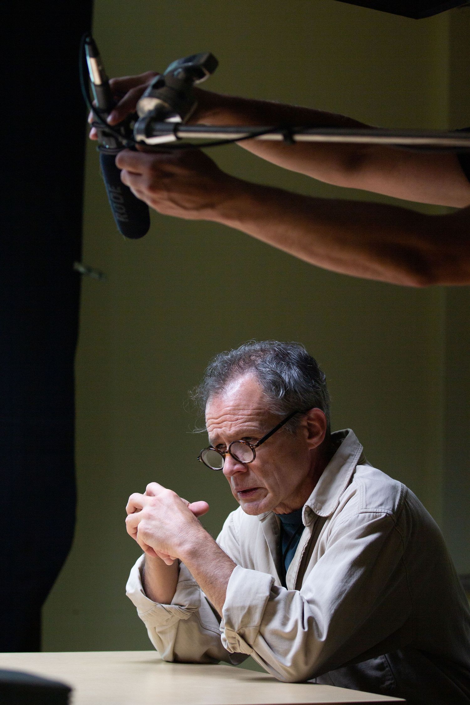 Person examining object under dramatic lighting with boom microphone visible.