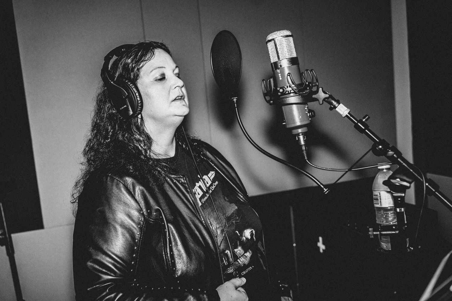 Black and white photo of vocalist recording in professional studio.