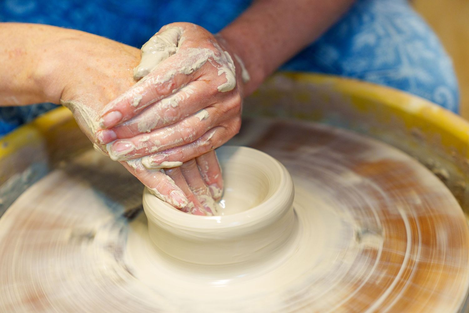 Close-up of hands shaping clay on a spinning pottery wheel with wet clay visible.