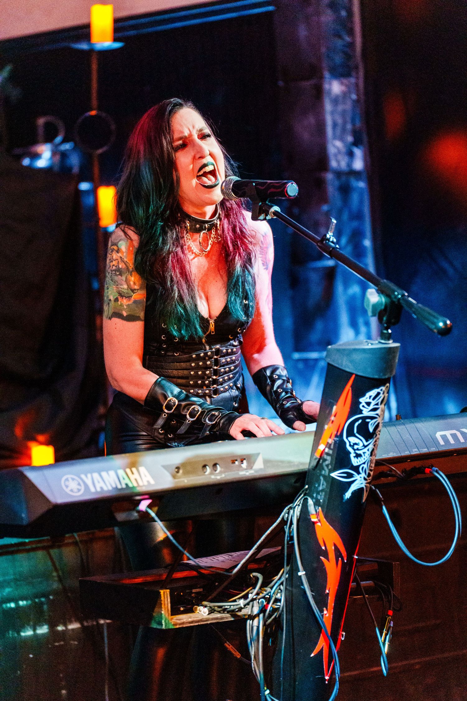 A musician performs at a keyboard on stage in dark lighting with dramatic blue and red stage lights.