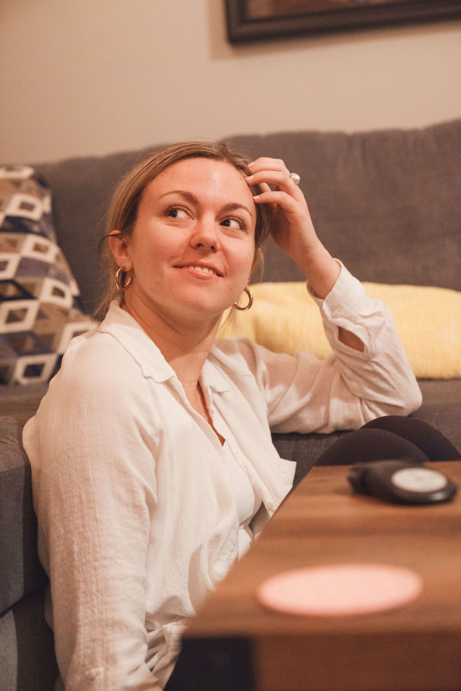 Person in white blouse relaxing on gray couch with thoughtful expression.