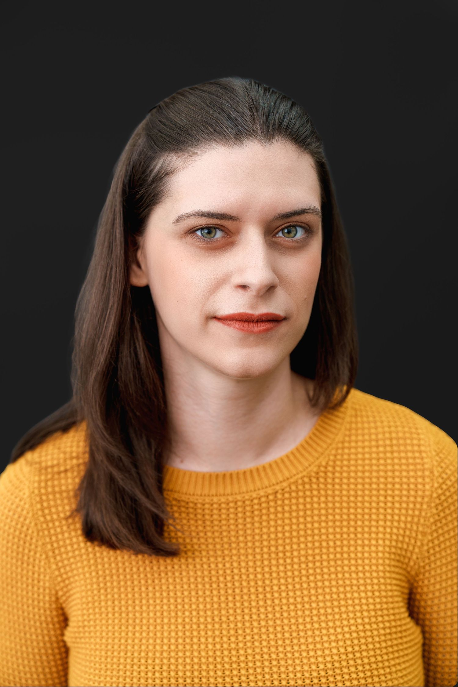 Professional headshot against dark background featuring yellow sweater and natural makeup.
