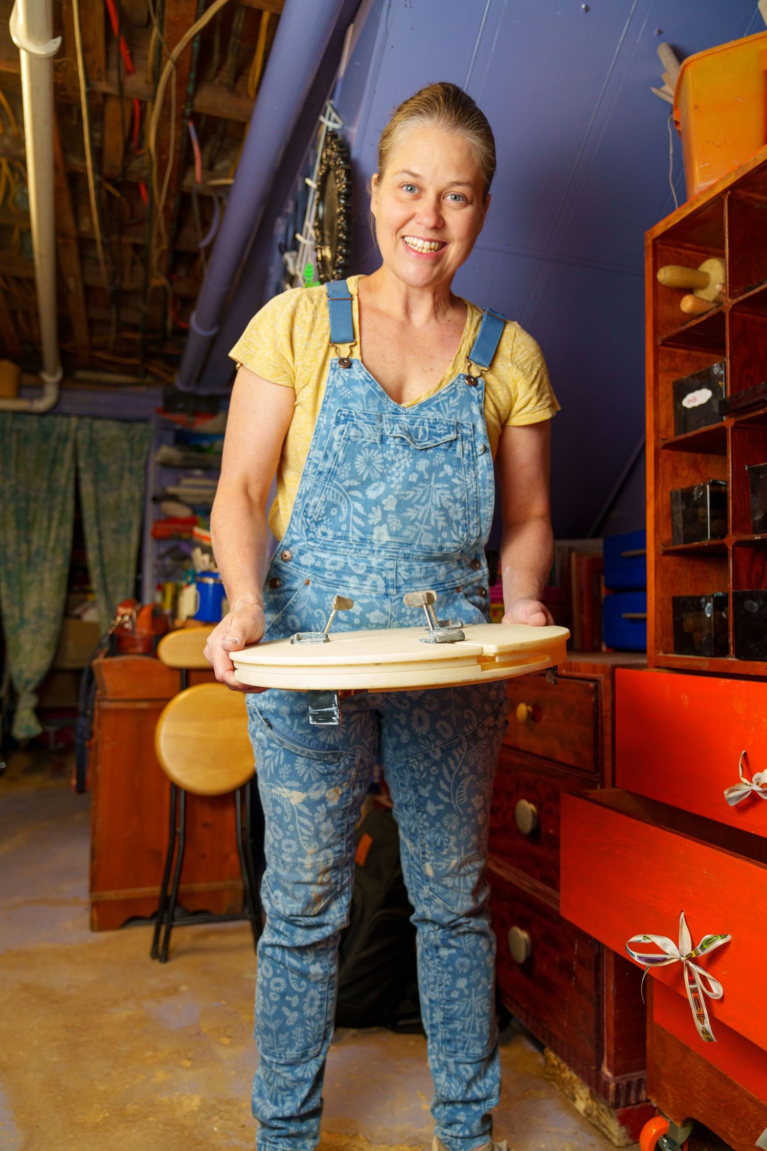 Person in blue overalls working with pottery materials in a craft studio setting.