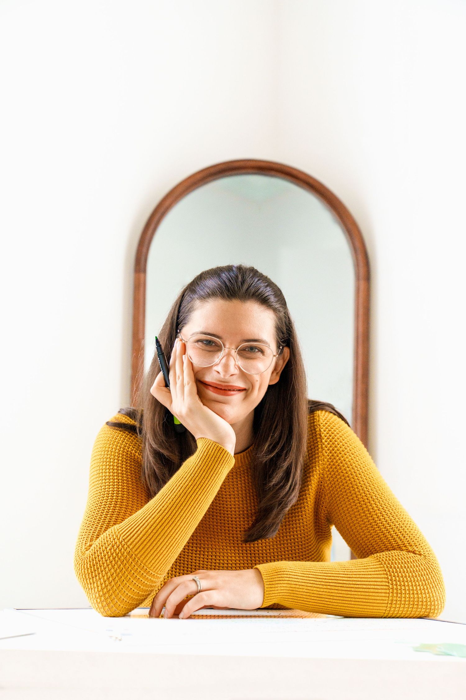 Person in yellow sweater and glasses posing near arched mirror.