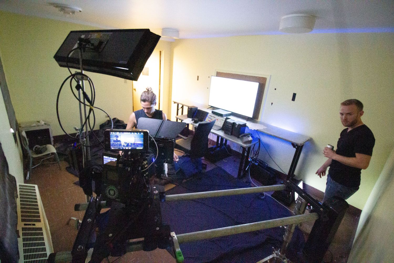 Professional film crew setting up camera equipment in a dimly lit room during a video production shoot.