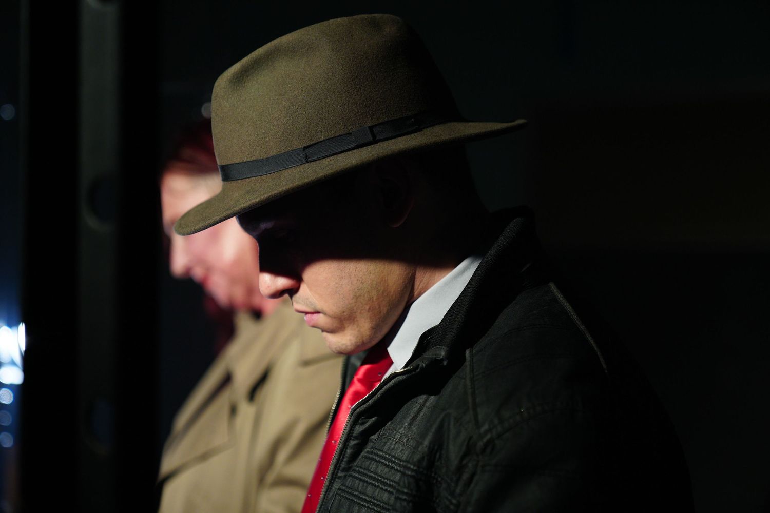 Man in vintage fedora hat and red tie in dramatic shadow lighting.