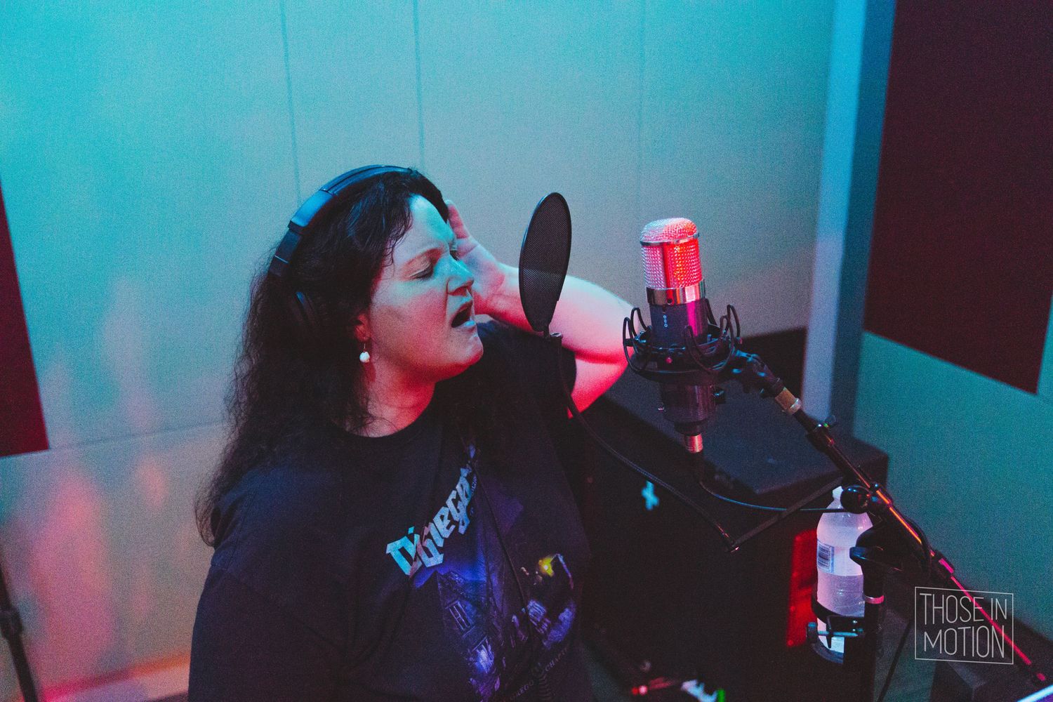 Singer recording vocals in studio with dramatic blue and red lighting.