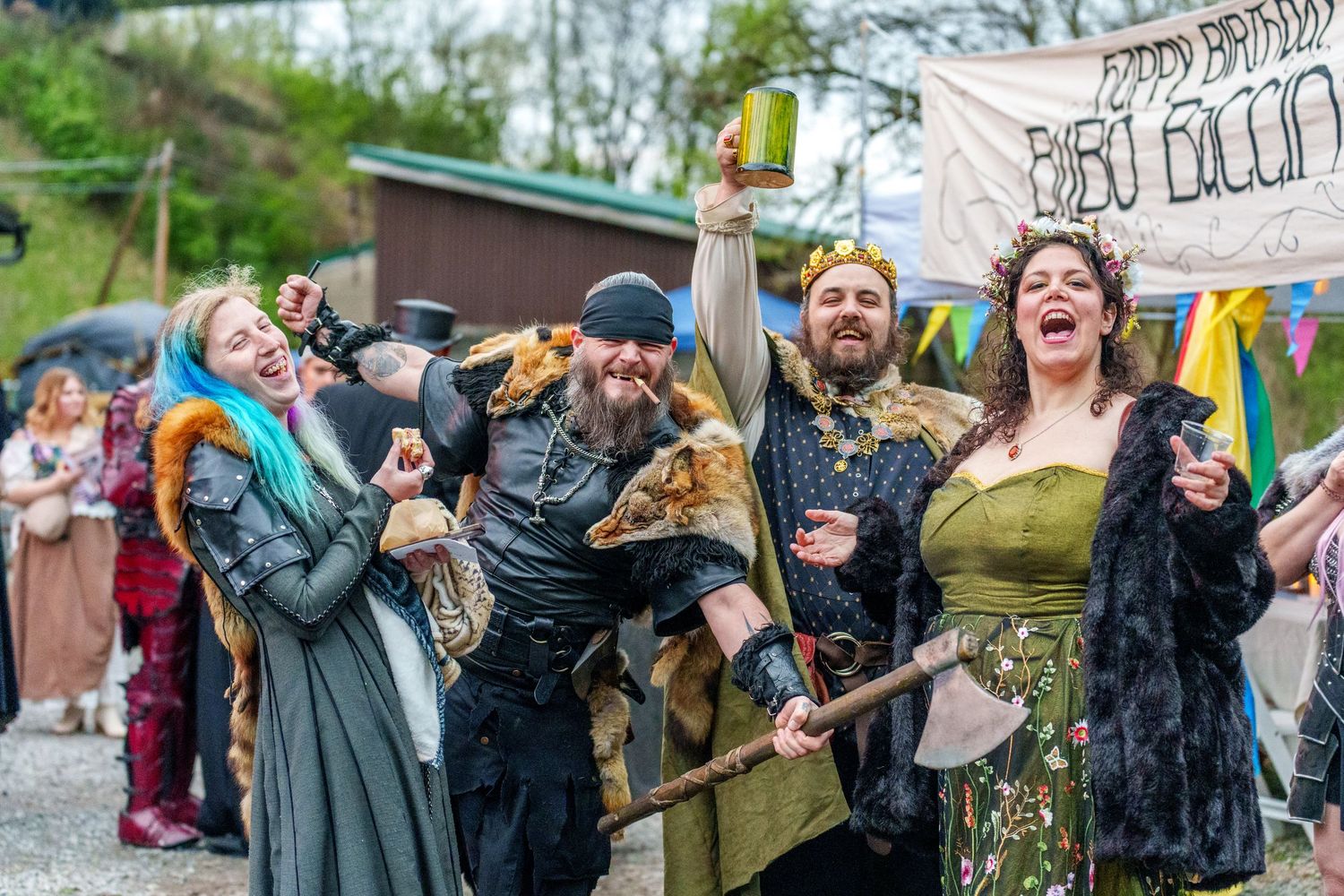 Costumed performers celebrate at a medieval renaissance fair with banners and period attire.
