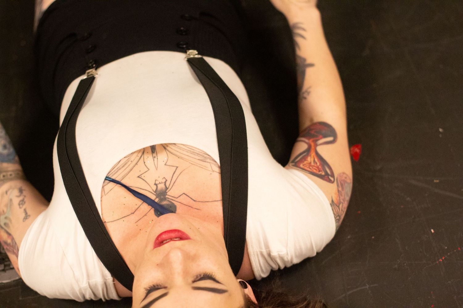 Dramatic overhead shot of performer with striking makeup lying on dark stage.