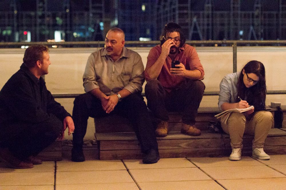 Four people sitting on outdoor steps at night, engaged in conversation and using phones.