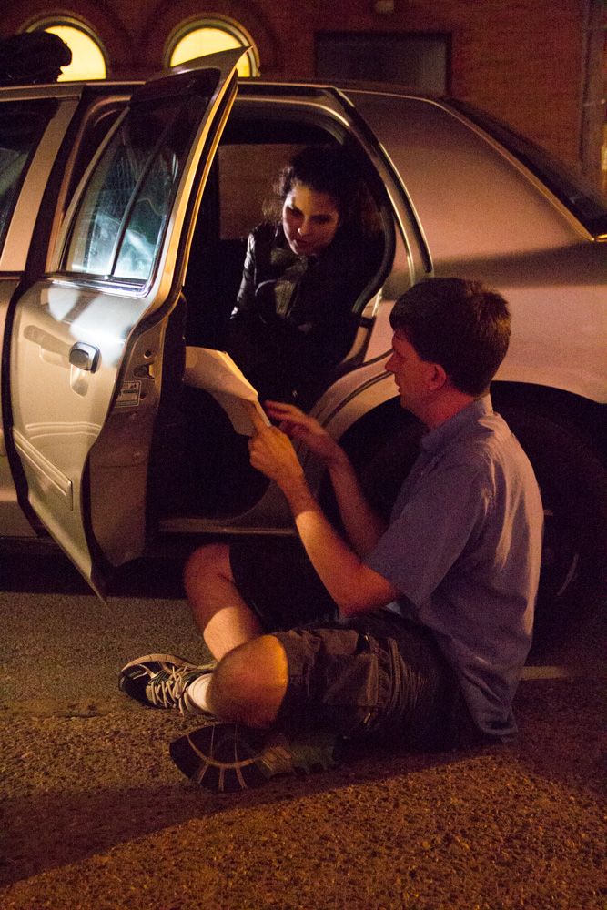 Man sitting on ground reads document handed by person in car door at night.